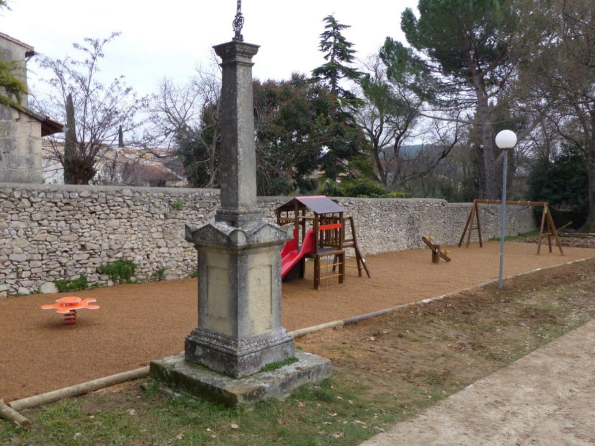 L'aire de jeux du village, toboggan et balançoires près d'un ancien monument de pierre.