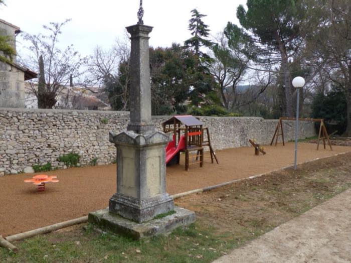 L'aire de jeux du village, toboggan et balançoires près d'un ancien monument de pierre.