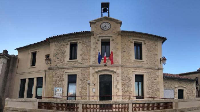 La mairie de Lecques, façade en pierre à deux niveaux surmontée d'une horloge et d'un campanile, drapeaux au balcon.