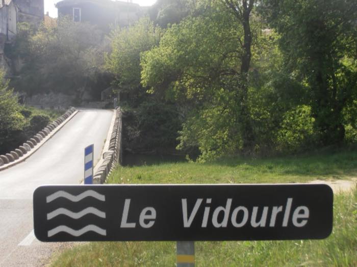 Le panneau routier « Le Vidourle » planté au bord de la chaussée, juste avant le pont.