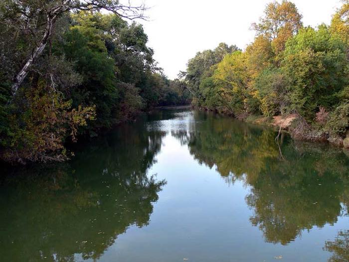 Le Vidourle en eaux calmes, bordé d'arbres dont le feuillage se reflète à la surface.